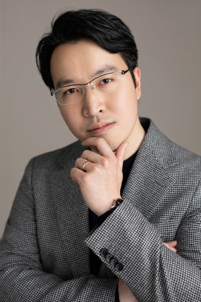Ed Hung, hand to chin, in a grey houndstooth blazer